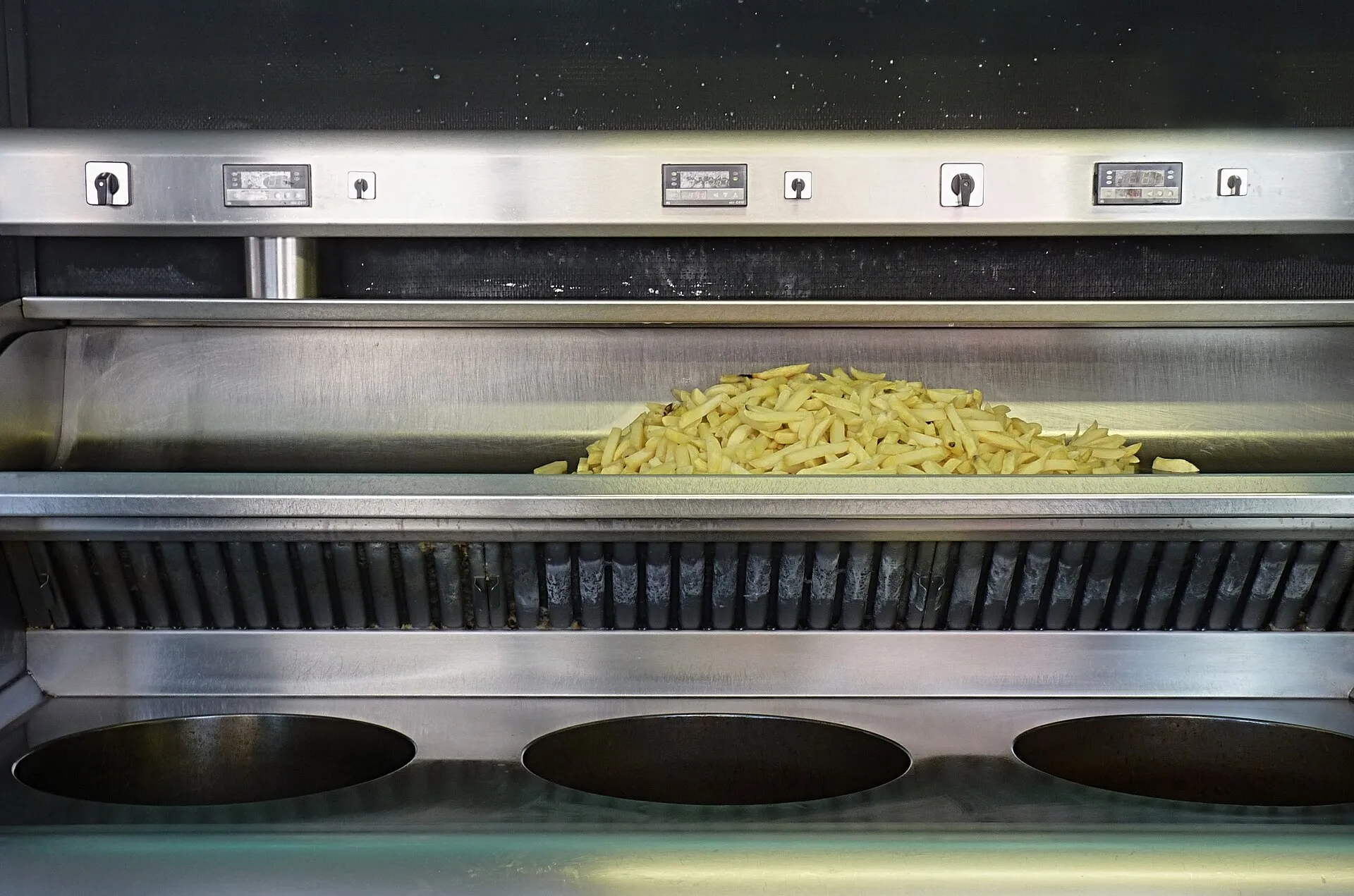 Chips beside the frying baskets of a commercial deep fat fryer